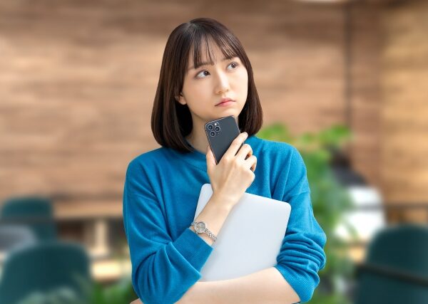 スマホをアゴに当てて斜め上を見つめながら考え込む女性