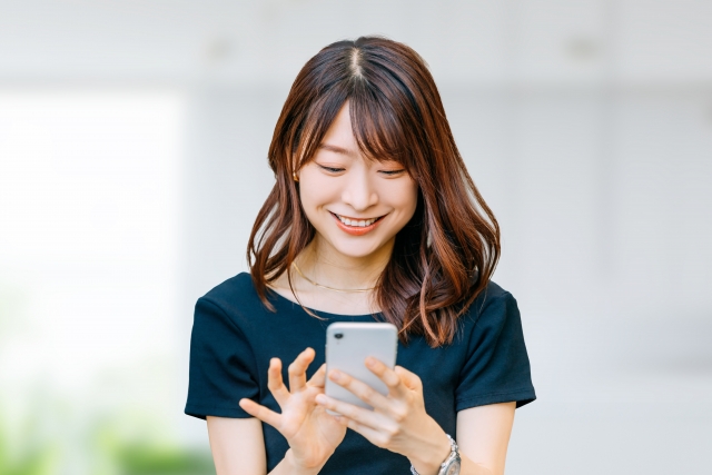 立った姿勢で両手でスマホを持ち、操作している笑顔の女性