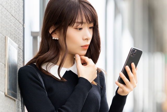 立って壁に寄りかかってスマホを見る女性