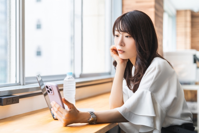 机に肘をついてスマホ画面を眺める女性