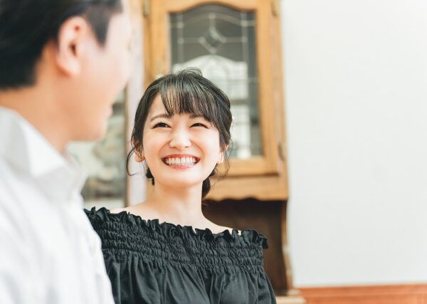 屋内で会話をするカップル。男性は向こう側を向いておりよく分からないが、女性はこちら向きで、男性に満面の笑みを浮かべている。