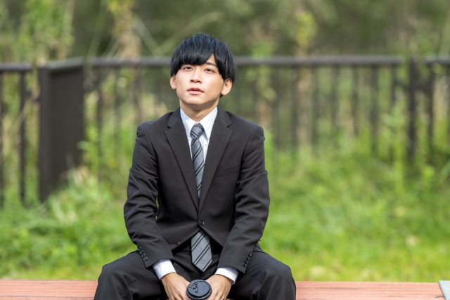 スーツ姿の男性がベンチに座り、前を見つめている