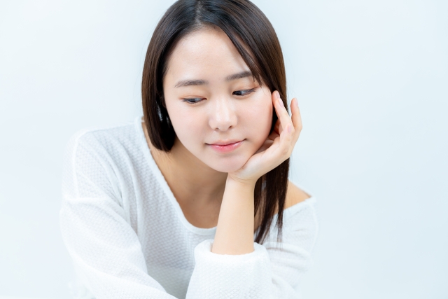 白いトップスを着た女性が頬杖をついて、微笑みながらうつむいている表情