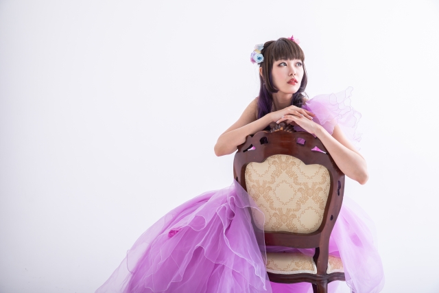 紫のドレスを着た女性が椅子越しに遠くを見つめている