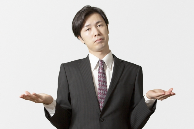 スーツ姿の男性が肩をすくめ、両手を広げて困った表情をしている。