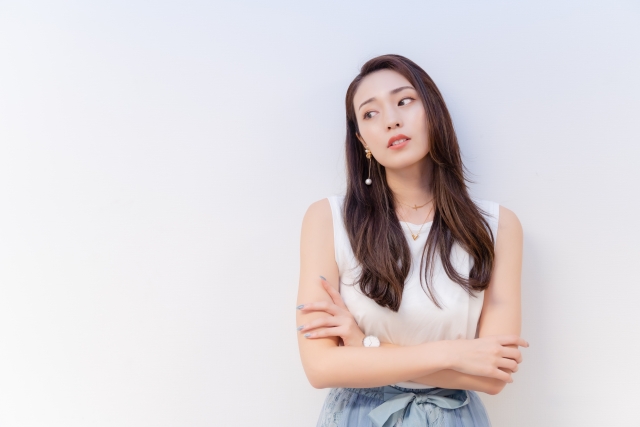 白い服の女性が腕を組み、壁にもたれて冷めた視線をそらしている。