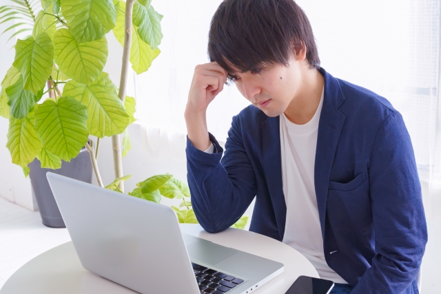 パソコンを前に考え込む男性が明るい部屋にいる。