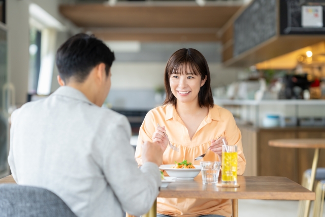 カフェで女性と向かい合って食事をする男女。女性は笑顔で会話を楽しんでいる。