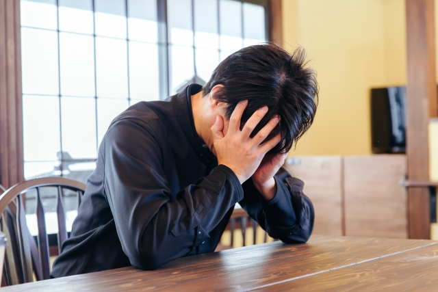 男性がテーブルにうつむき、両手で顔を覆って深く落ち込んでいる様子