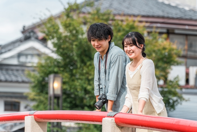 若い男女が橋の上で笑顔を見せながら並んで立ち、楽しそうに風景を眺めている。